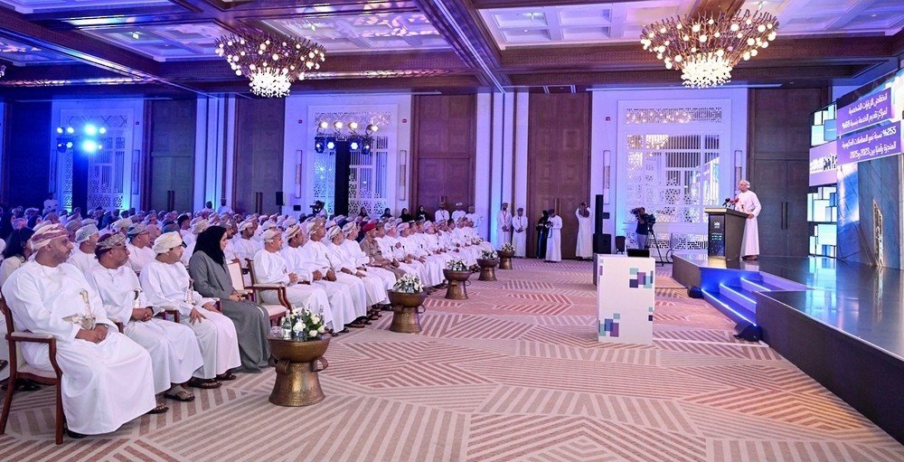 Rows of attendees in Omani dress listen to a speaker at a podium during a ceremony in a hotel ballroom