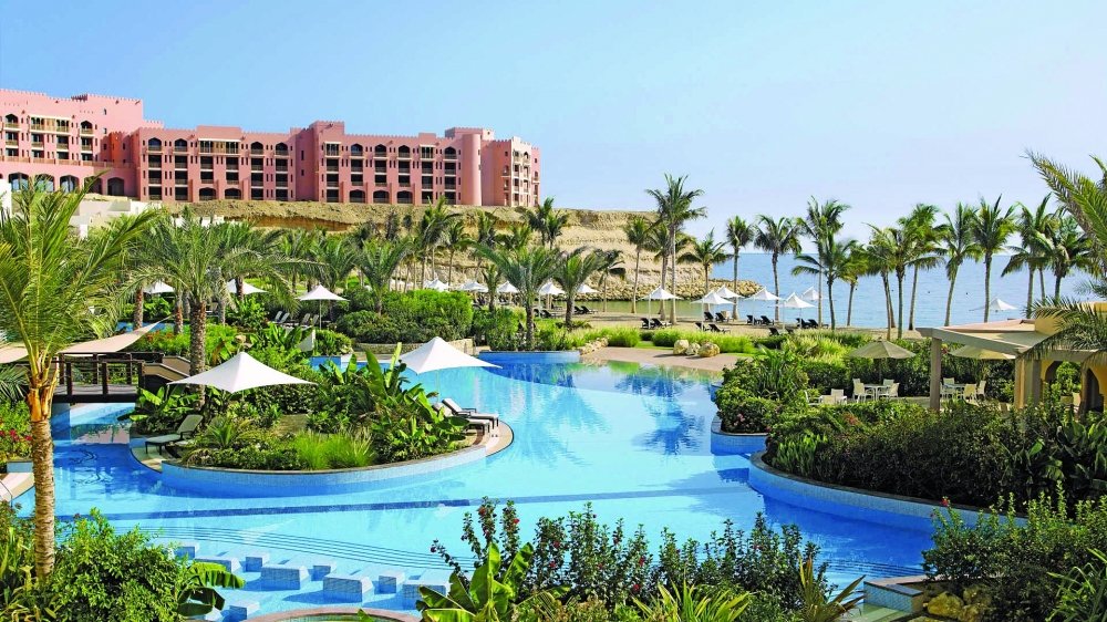 Pool, palm gardens and a pink hotel building at a beach resort on the Muscat coast in Oman