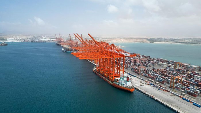 Orange ship-to-shore cranes over a container ship at a berth at an Omani port terminal