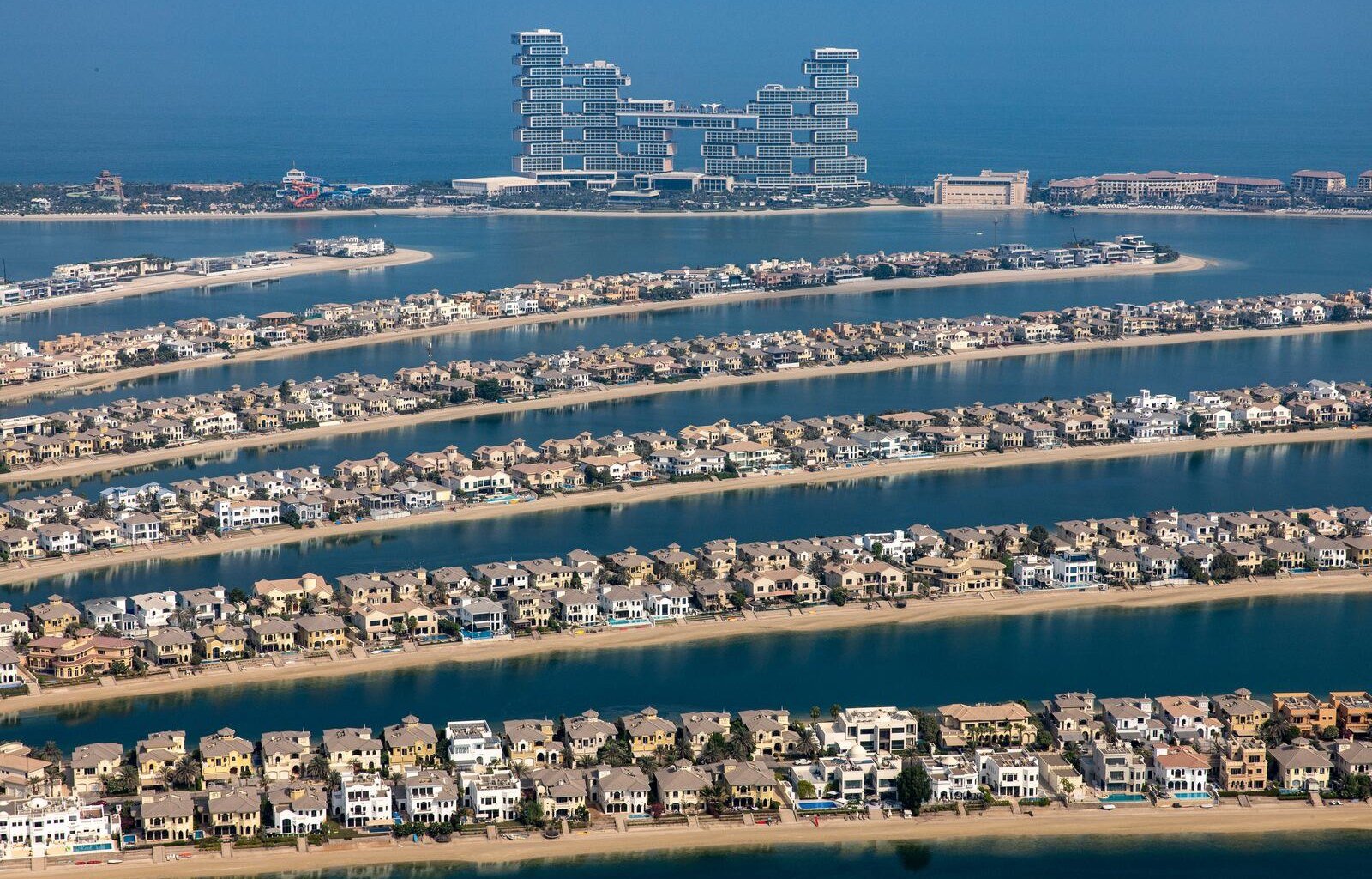 An aerial view of rows of waterfront villas on the fronds of Palm Jumeirah, with towers on the horizon