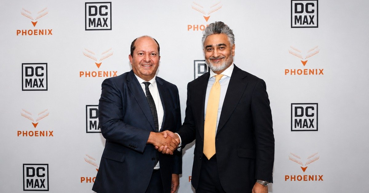 Romain Fremont of DC Max and Munaf Ali of Phoenix Group shake hands in front of a branded backdrop