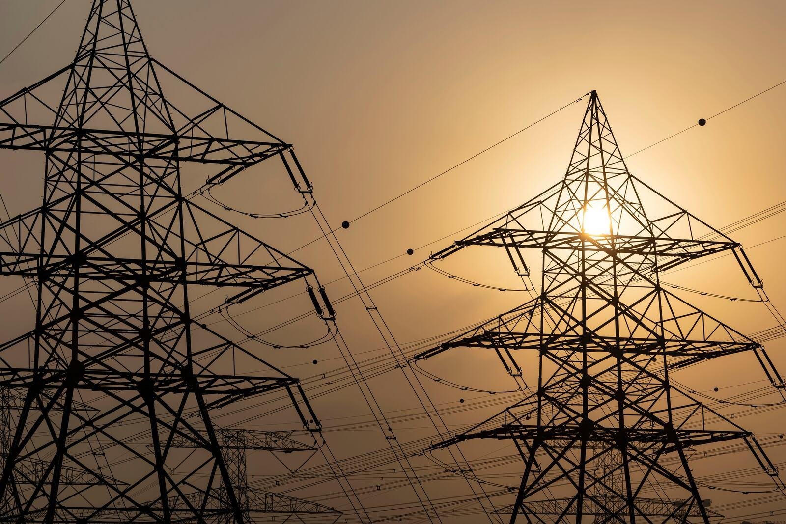 Electricity transmission towers and power lines against a hazy sun