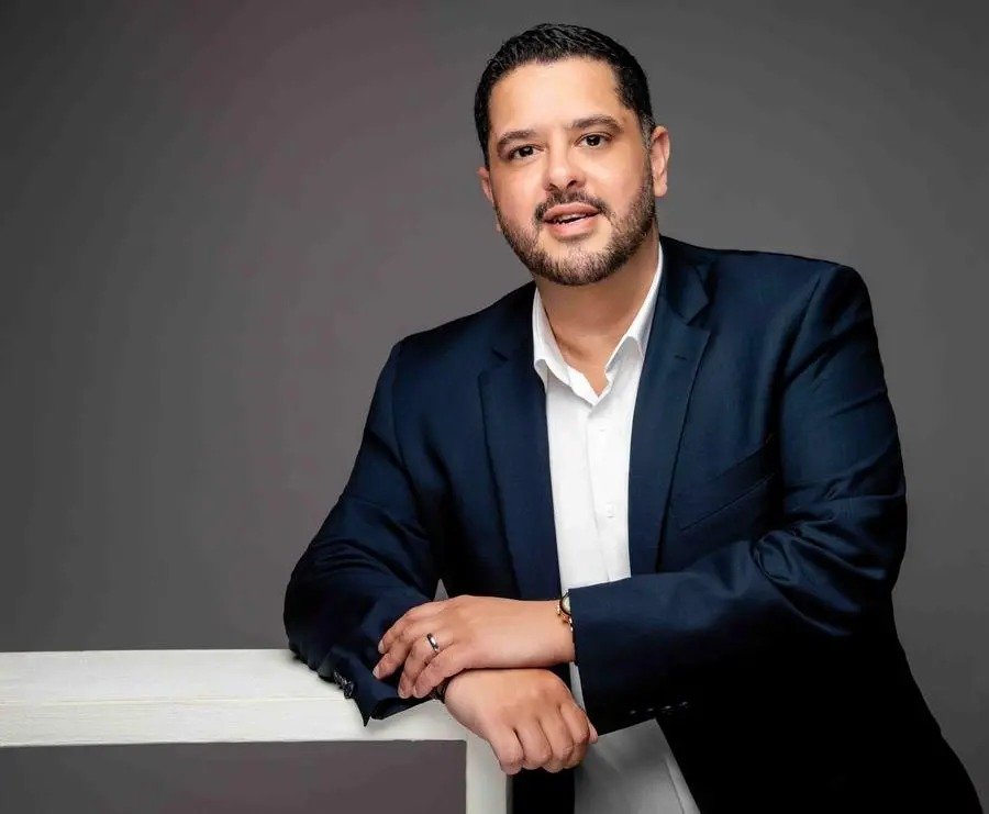 Qashio founder and chief executive Armin Moradi, wearing a navy suit, leans on a white ledge against a gray backdrop