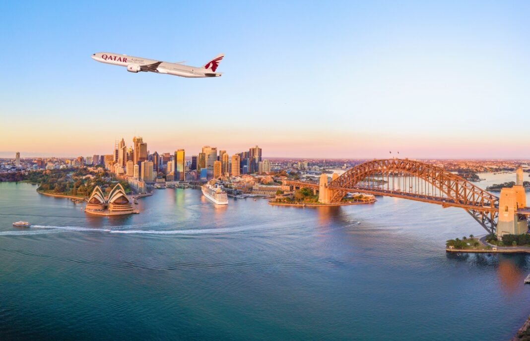 A Qatar Airways Boeing 777 in flight above Sydney Harbour, the Opera House and the Harbour Bridge at dusk
