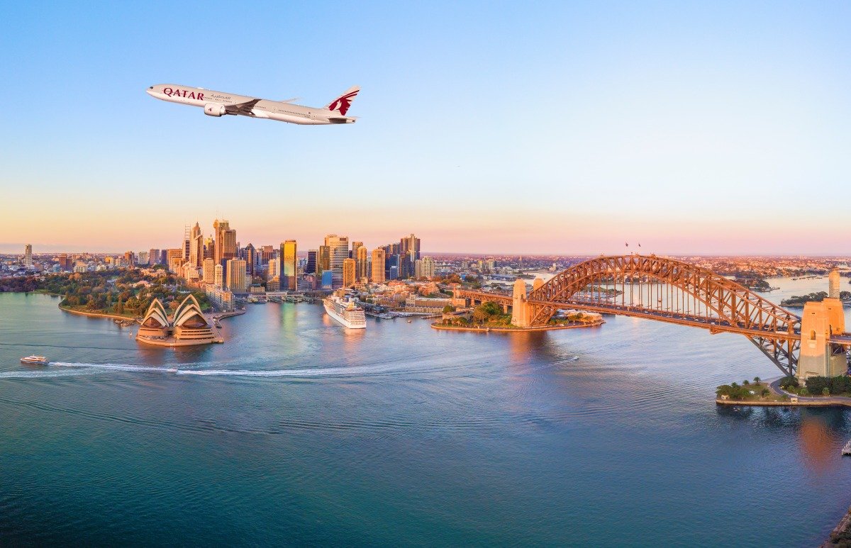 A Qatar Airways Boeing 777 in flight above Sydney Harbour, the Opera House and the Harbour Bridge at dusk