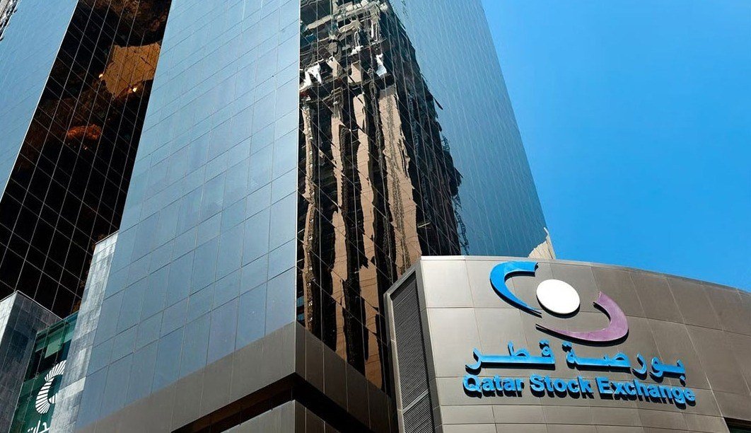 Qatar Stock Exchange logo on a curved building facade beside glass towers in Doha