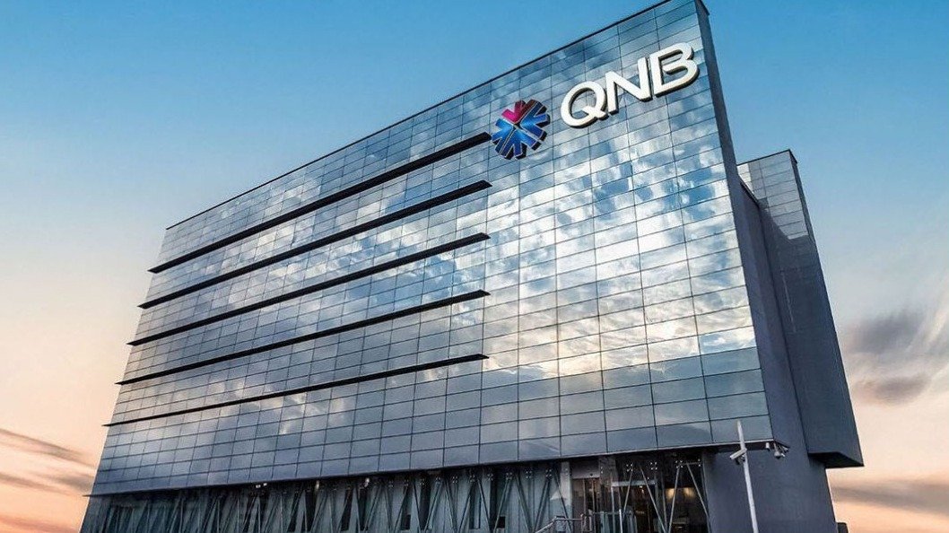A glass office tower with the QNB logo near the top, against an evening sky