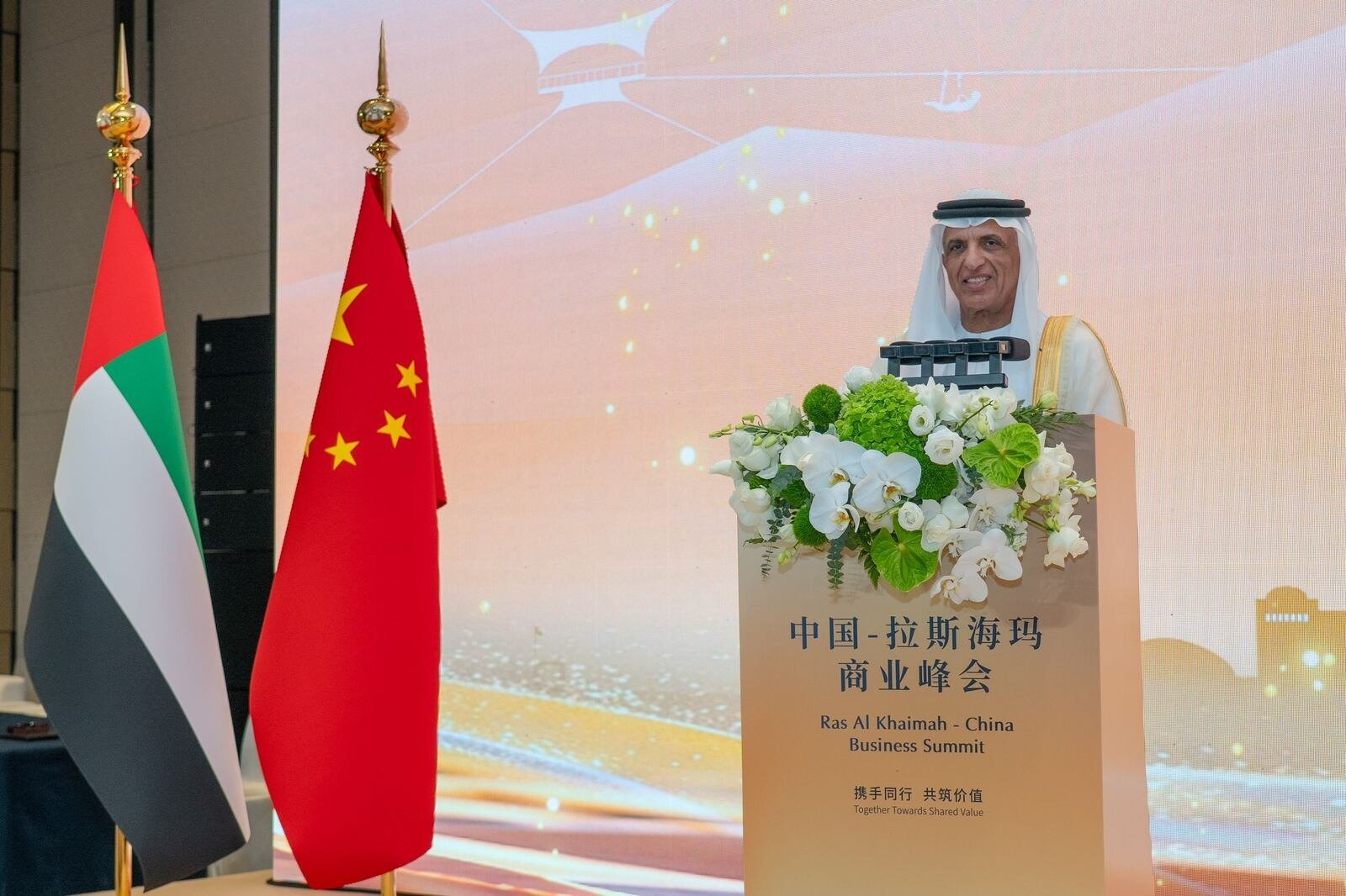 Ras Al Khaimah Ruler Sheikh Saud bin Saqr Al Qasimi speaks at a podium between UAE and Chinese flags at the Ras Al Khaimah-China Business Summit