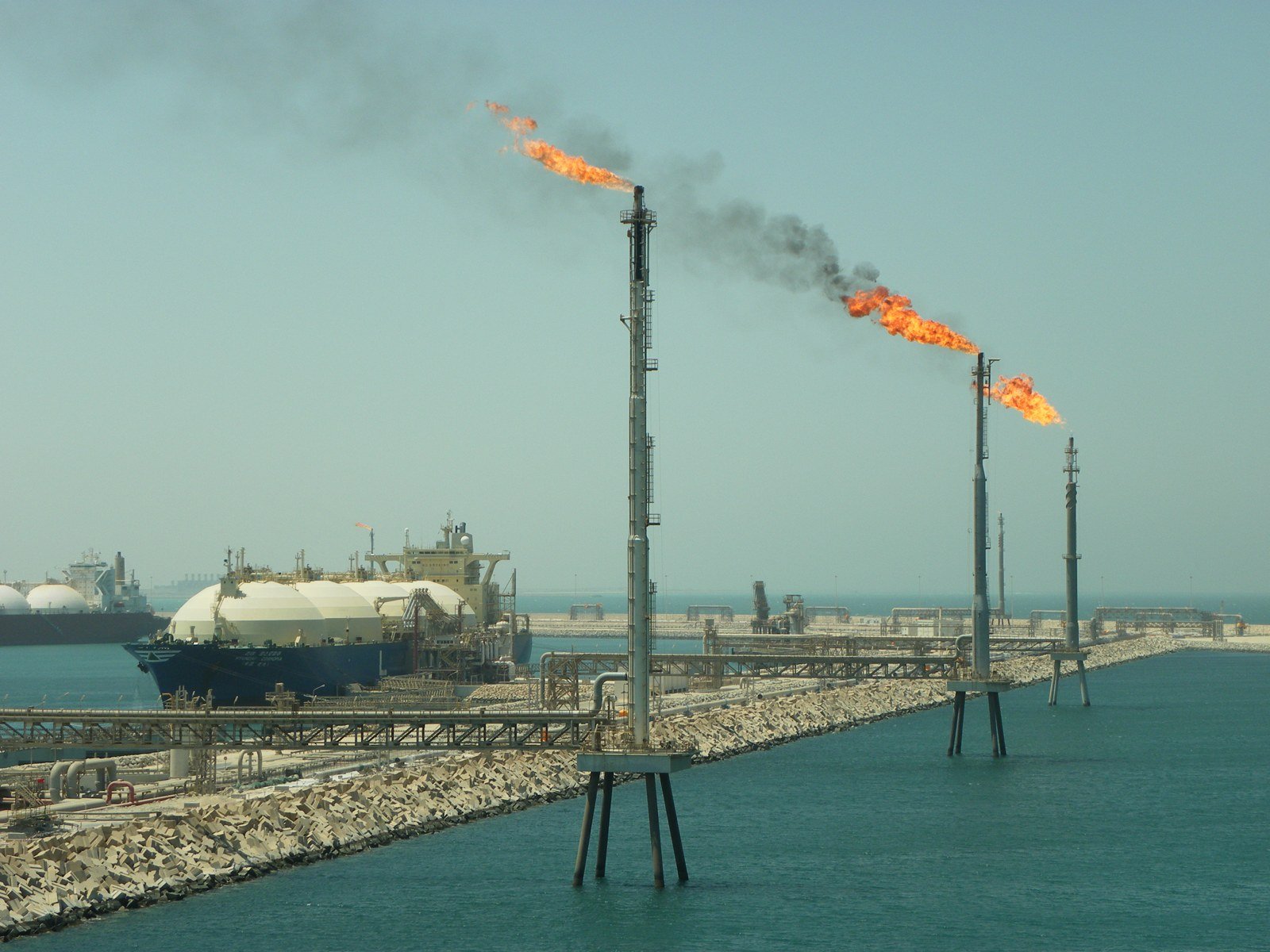 An LNG carrier moored at the Ras Laffan LNG terminal in Qatar with gas flares burning on offshore stacks