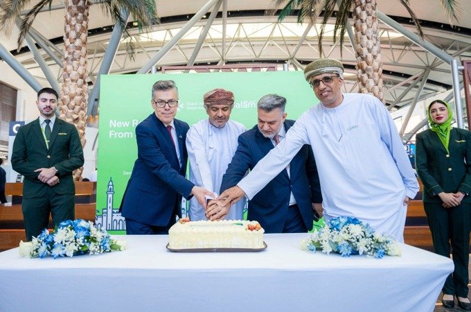 Officials in suits and Omani dress cut a cake together at Muscat International Airport as SalamAir cabin crew stand beside them