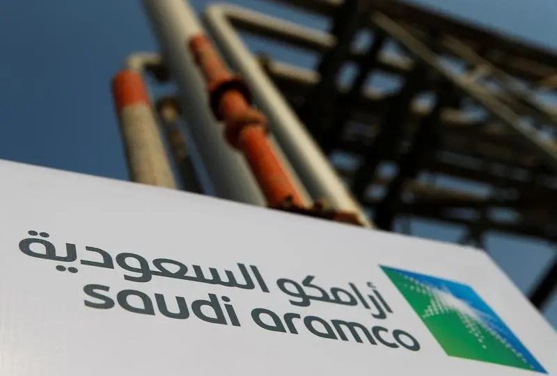 A Saudi Aramco sign in Arabic and English in front of pipework at the company's oil facility in Abqaiq, Saudi Arabia