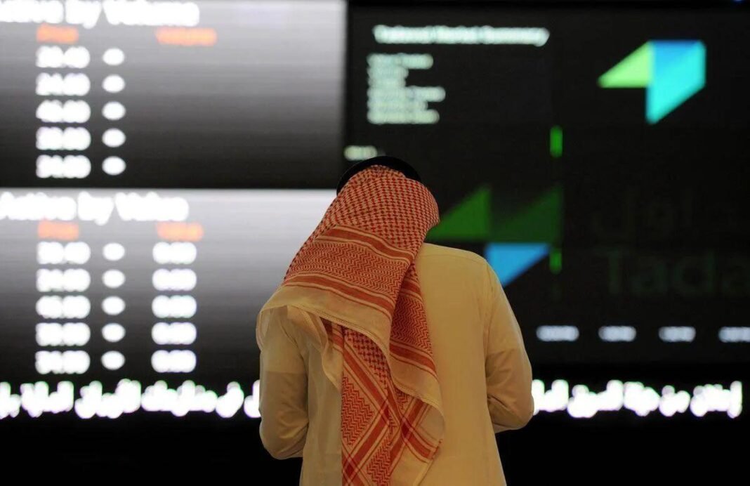 A man in a red checkered headscarf looks at trading screens at the Saudi Exchange
