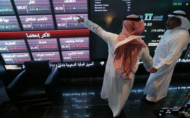 Two men point at share price screens at the Saudi Exchange in Riyadh