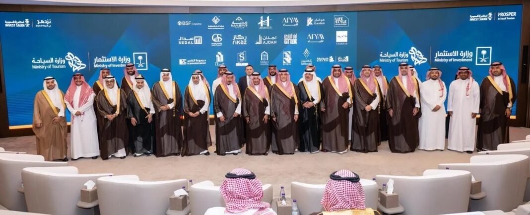A group of officials in traditional Saudi dress stand in front of a screen showing the logos of the Ministry of Tourism, the Ministry of Investment and participating companies