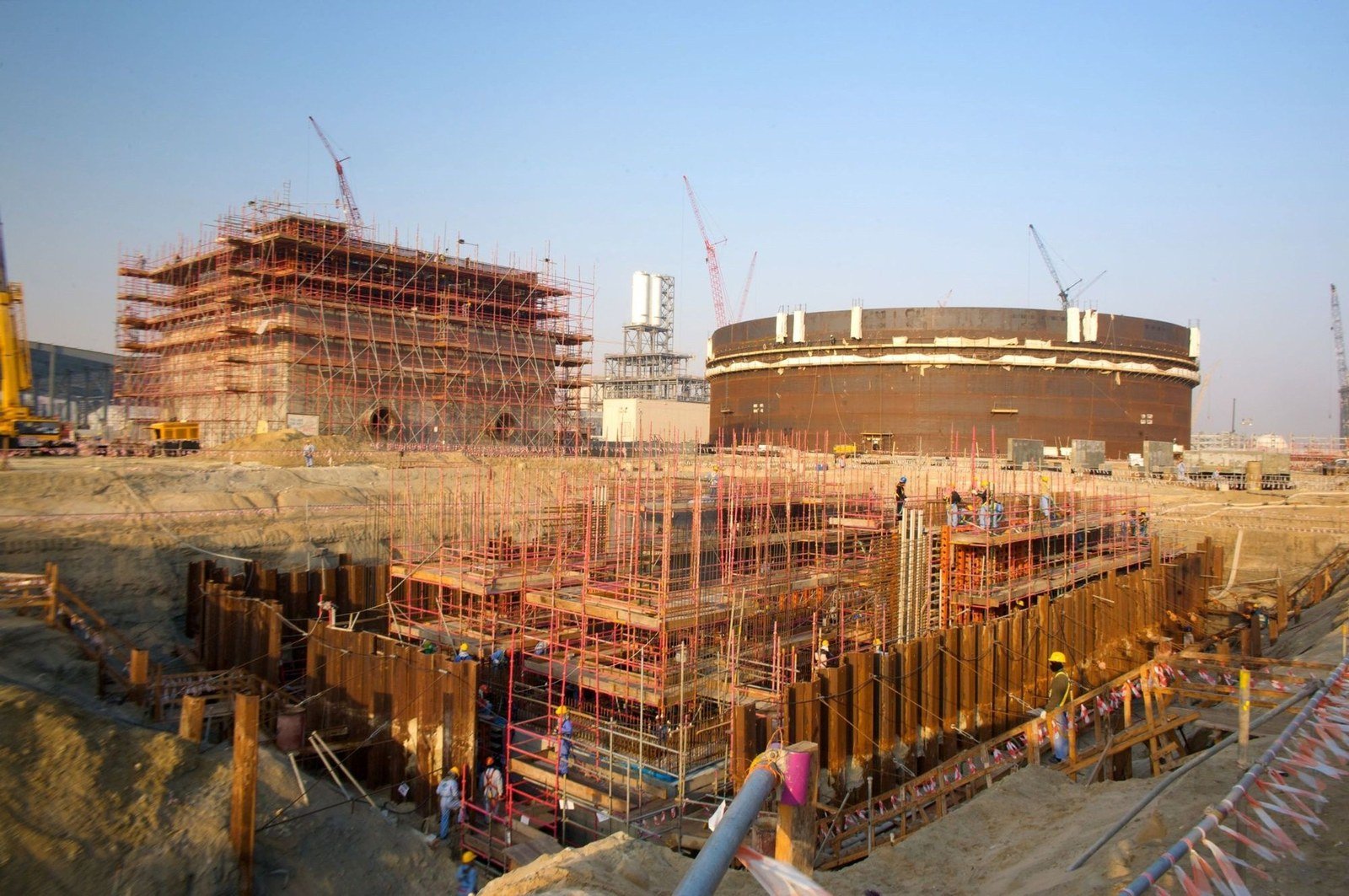 Scaffolding and construction cranes surround concrete structures and a large circular tank at the Saudi Kayan petrochemical complex site in Jubail