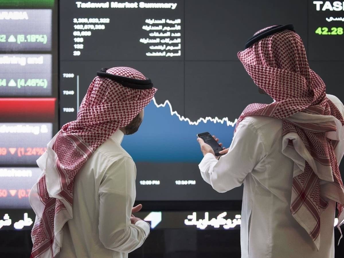Two men in traditional Saudi dress look at a Tadawul market summary screen in Riyadh