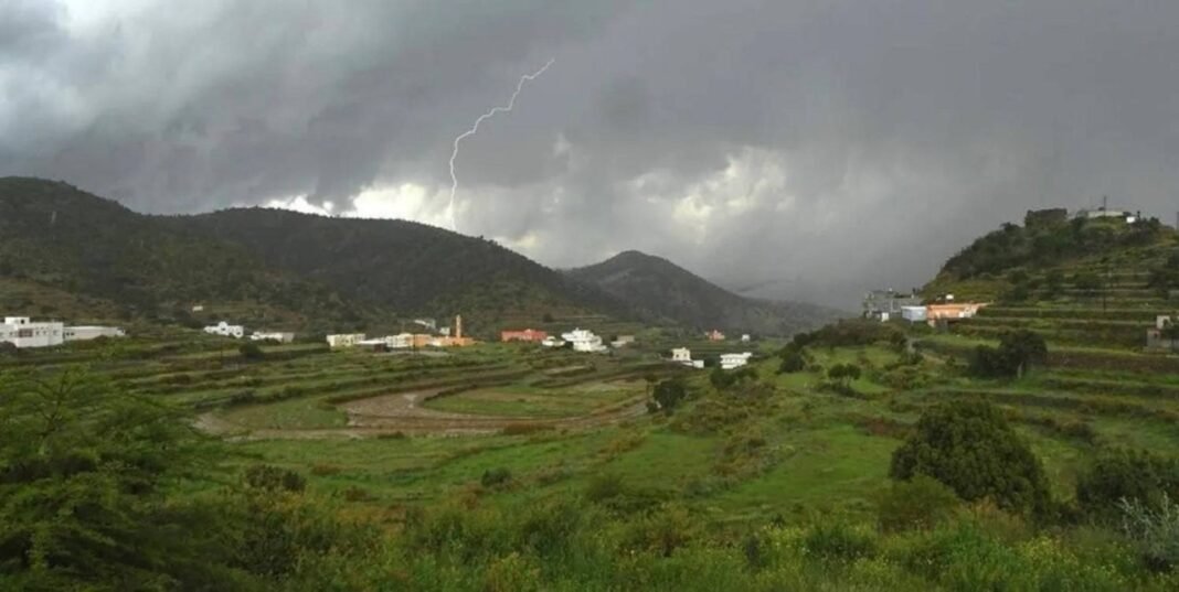Green terraced farmland and scattered houses in a mountainous area of Saudi Arabia under dark storm clouds