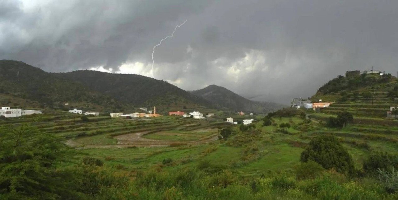 Green terraced farmland and scattered houses in a mountainous area of Saudi Arabia under dark storm clouds