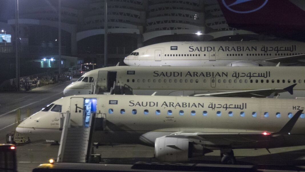 Three Saudi Arabian Airlines passenger jets parked at night beside a terminal at King Khalid International Airport in Riyadh