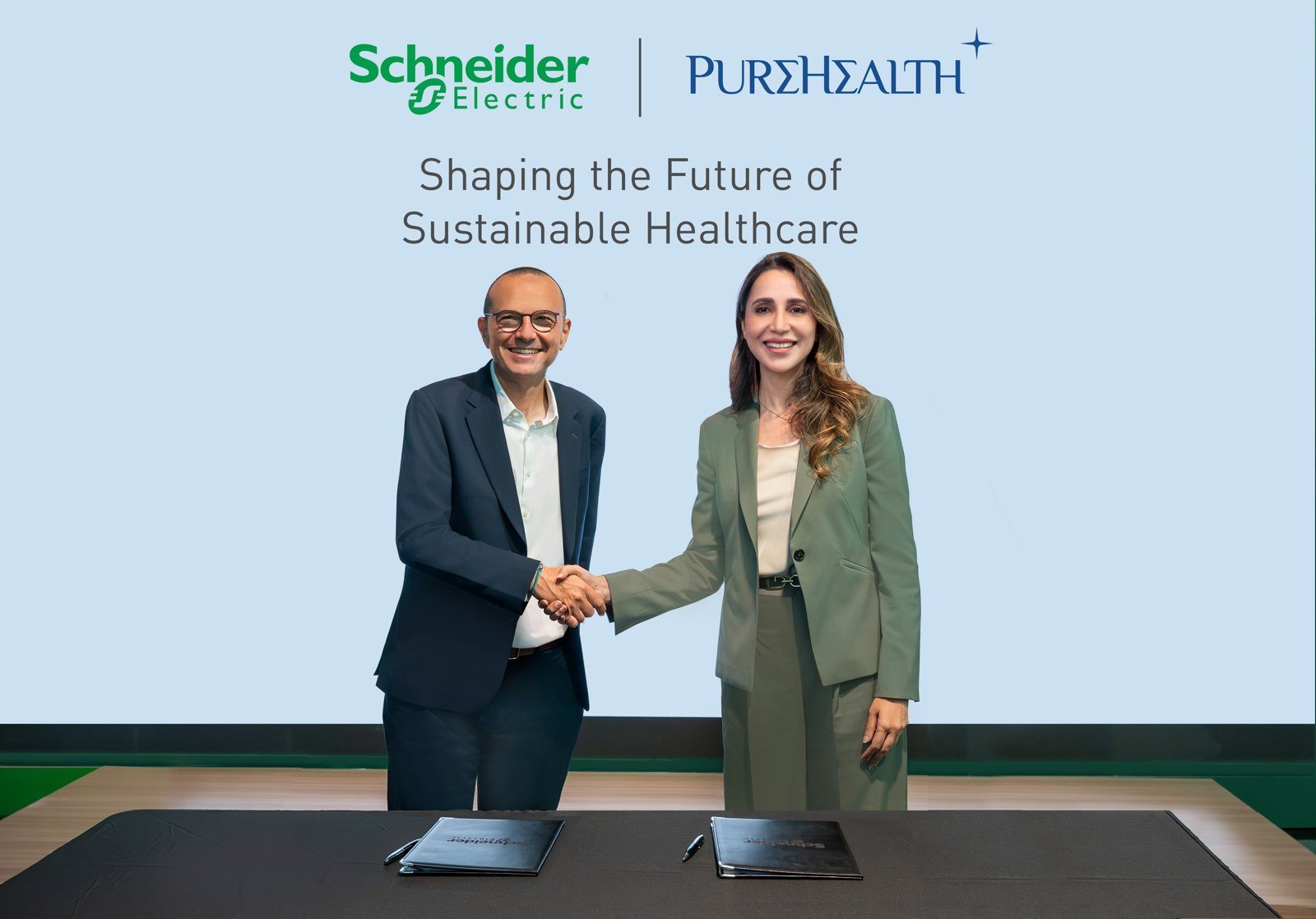 Schneider Electric and PureHealth executives shake hands at the signing of their sustainability partnership