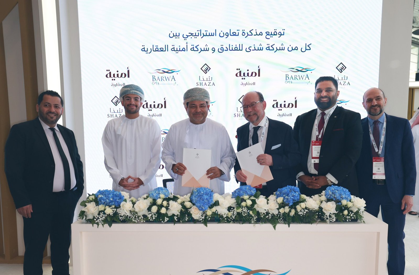 Executives of Shaza Hotels and Omnia Properties hold signed documents behind a table at the Barwa stand at Cityscape Qatar