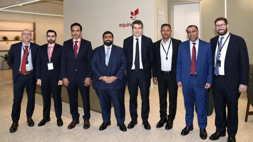 Eight men in dark business suits stand in a row in an office lobby in front of a wall bearing the Equinor name and logo