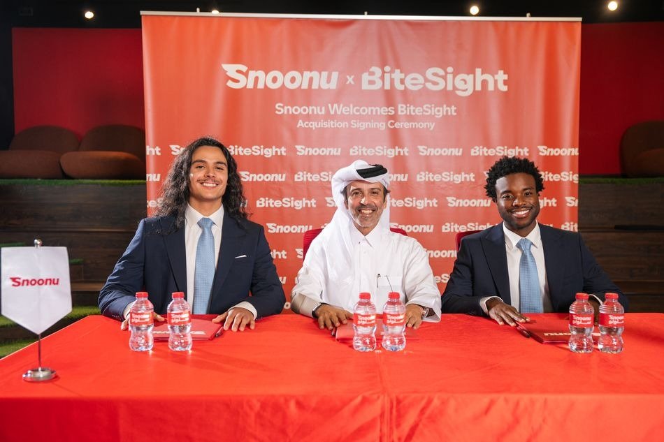 Three men seated at a red table in front of a Snoonu and BiteSight acquisition signing ceremony backdrop