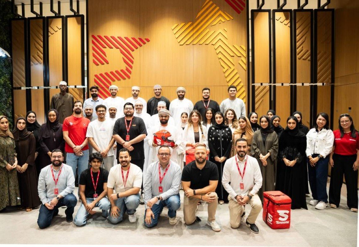 Snoonu employees pose for a group photo in front of a wall with the company's red and yellow emblem
