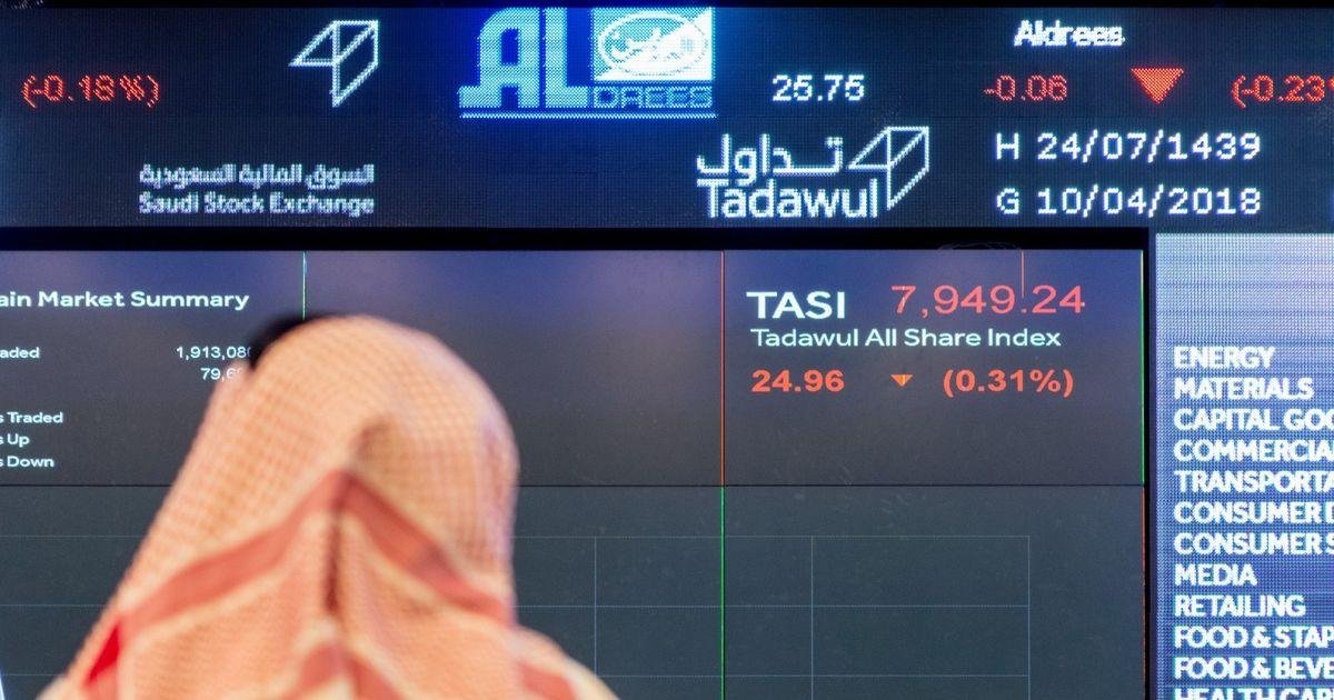 A man looks at a Saudi Exchange screen showing the Tadawul All Share Index