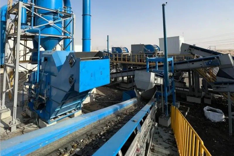 Blue recycling machinery, a dust collection tower and conveyor belts carrying shredded material at an outdoor plant under a clear sky