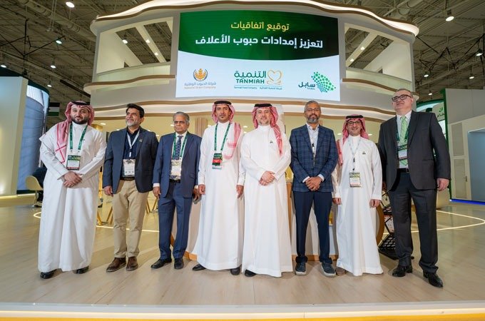 A group of executives standing in front of a stand with a screen showing the Tanmiah, Sabil and National Grain Company logos at an exhibition in Riyadh