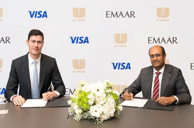 Two men in suits signing documents at a table in front of a backdrop with Visa, Emaar and U by Emaar logos