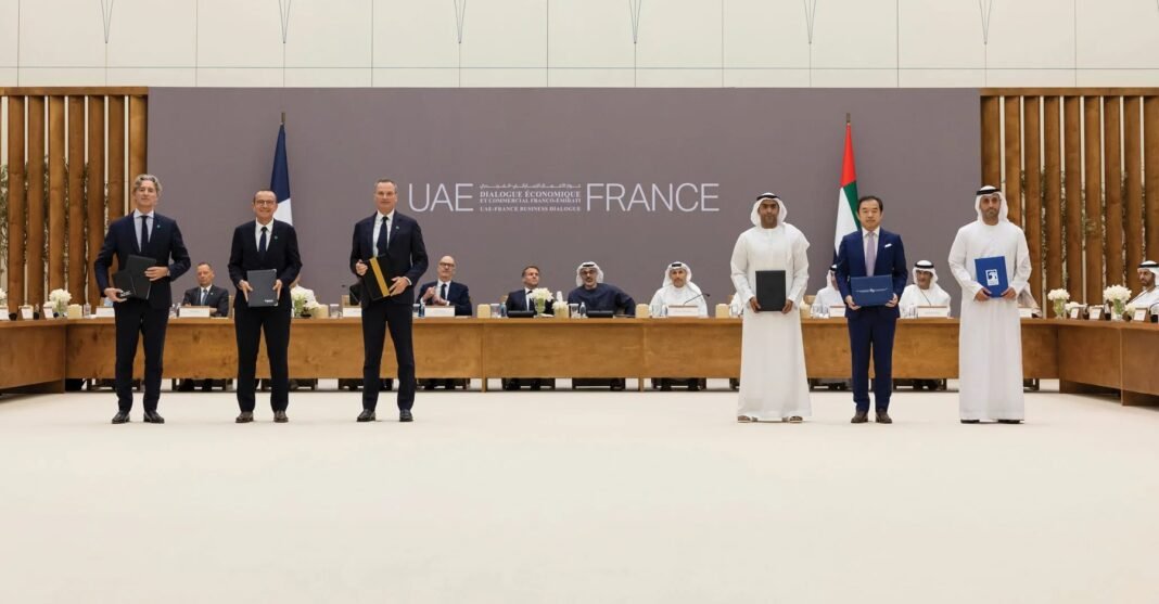 Six executives standing in front of a UAE France backdrop holding signed agreement folders, with officials seated at a long table behind them