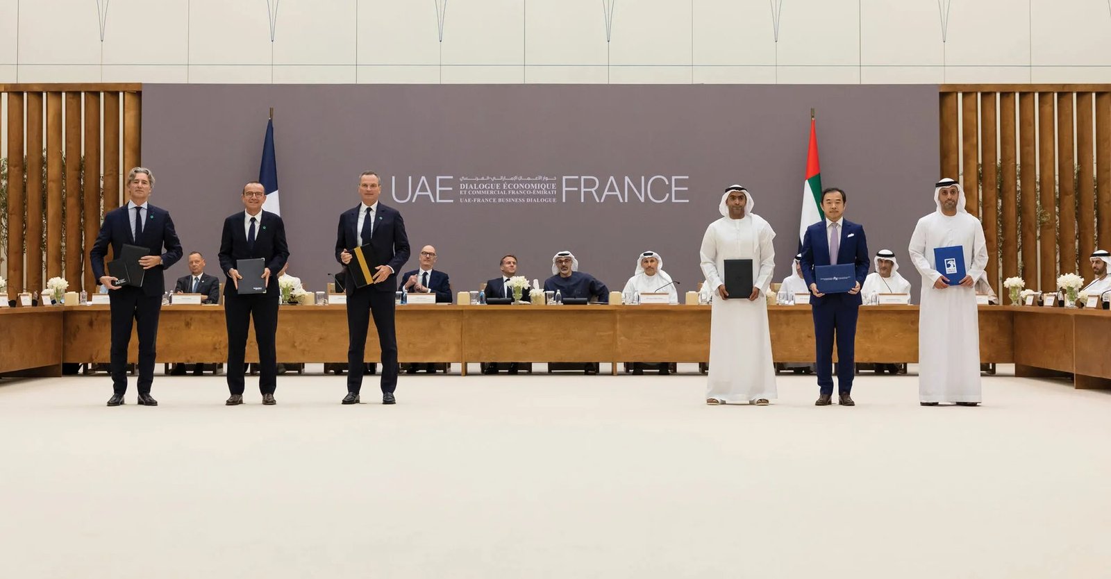 Six executives standing in front of a UAE France backdrop holding signed agreement folders, with officials seated at a long table behind them