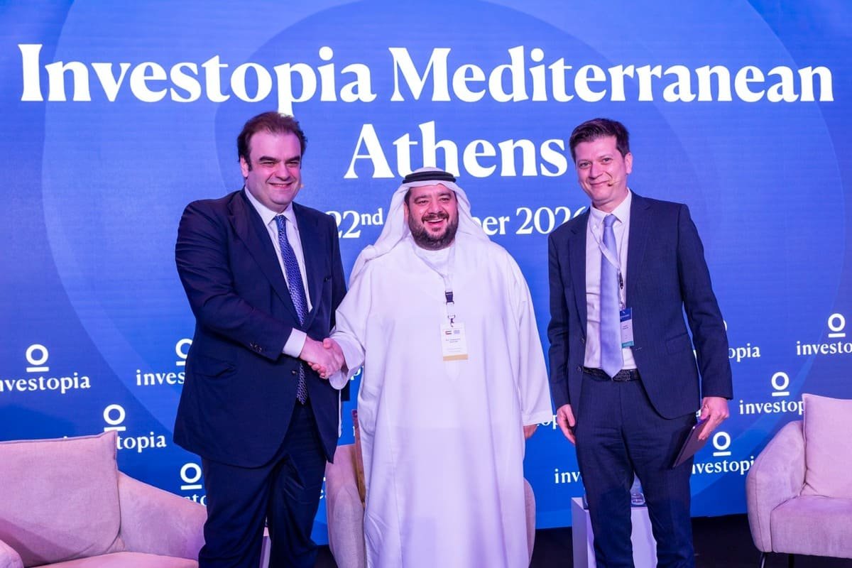 Three men shaking hands on stage in front of an Investopia Mediterranean Athens backdrop