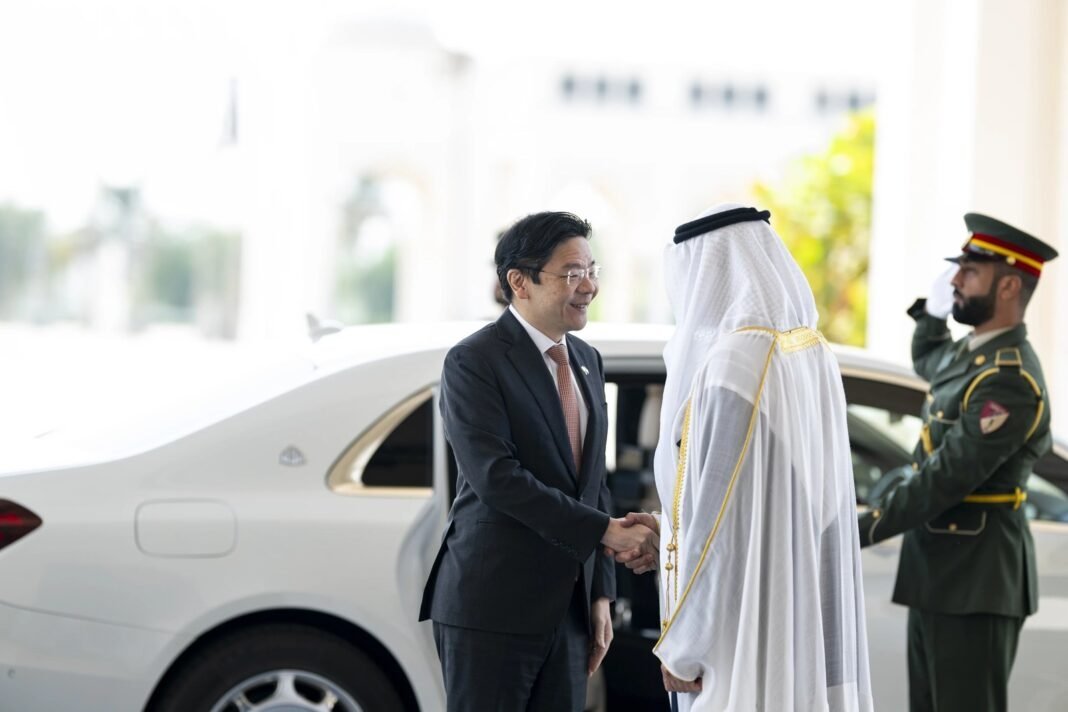 Singapore Prime Minister Lawrence Wong in a dark suit shakes hands with UAE President Sheikh Mohamed bin Zayed in white robes beside a car, as an honor guard salutes
