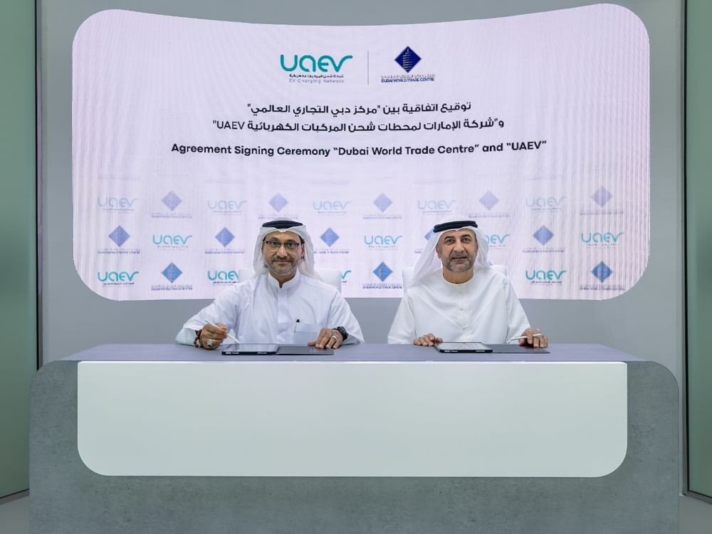 Two executives in white kanduras signing documents at a table in front of a screen reading Agreement Signing Ceremony Dubai World Trade Centre and UAEV