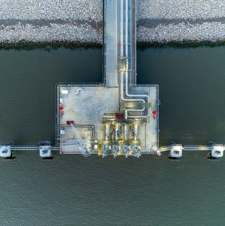 Aerial view of an LNG loading platform with pipework on a jetty over water