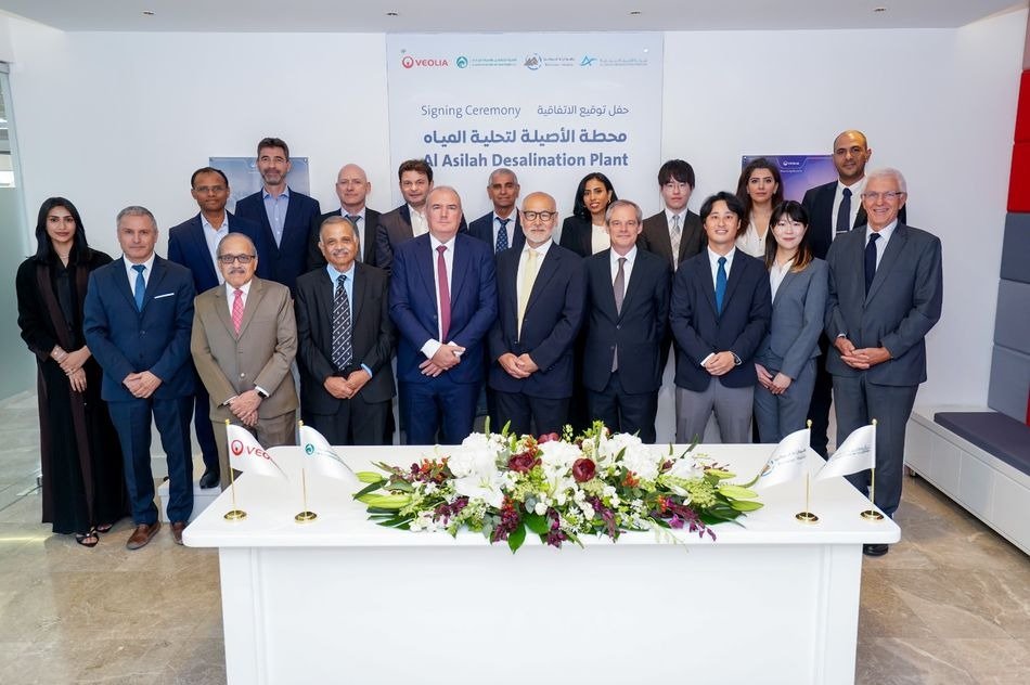 A group of executives standing behind a signing table with flowers in front of an Al Asilah Desalination Plant signing ceremony banner