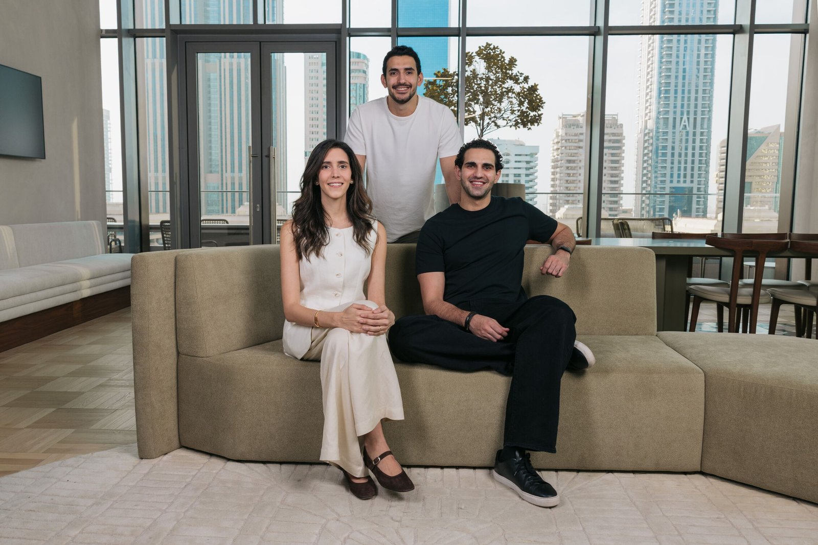 Ziina co-founders Faisal, Sarah and Talal Toukan seated on a sofa in an office overlooking Dubai towers